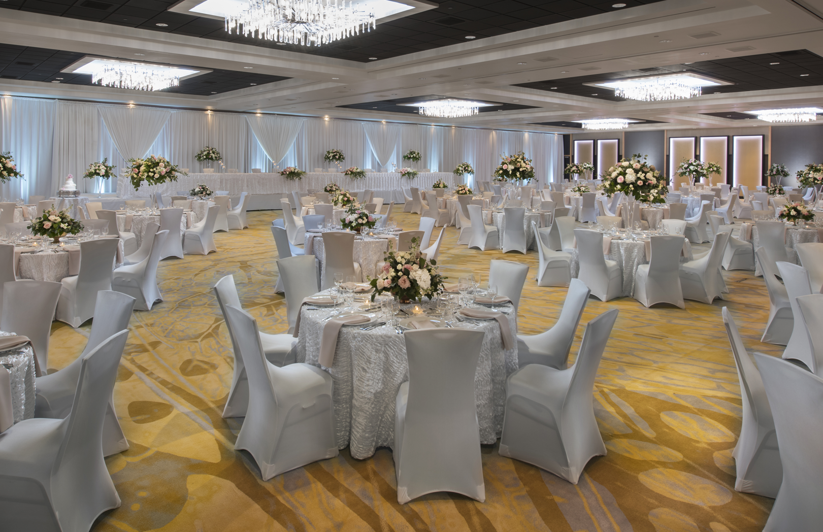 Wedding reception setup with white tablecloths, chair covers, and floral centerpieces in the convention center