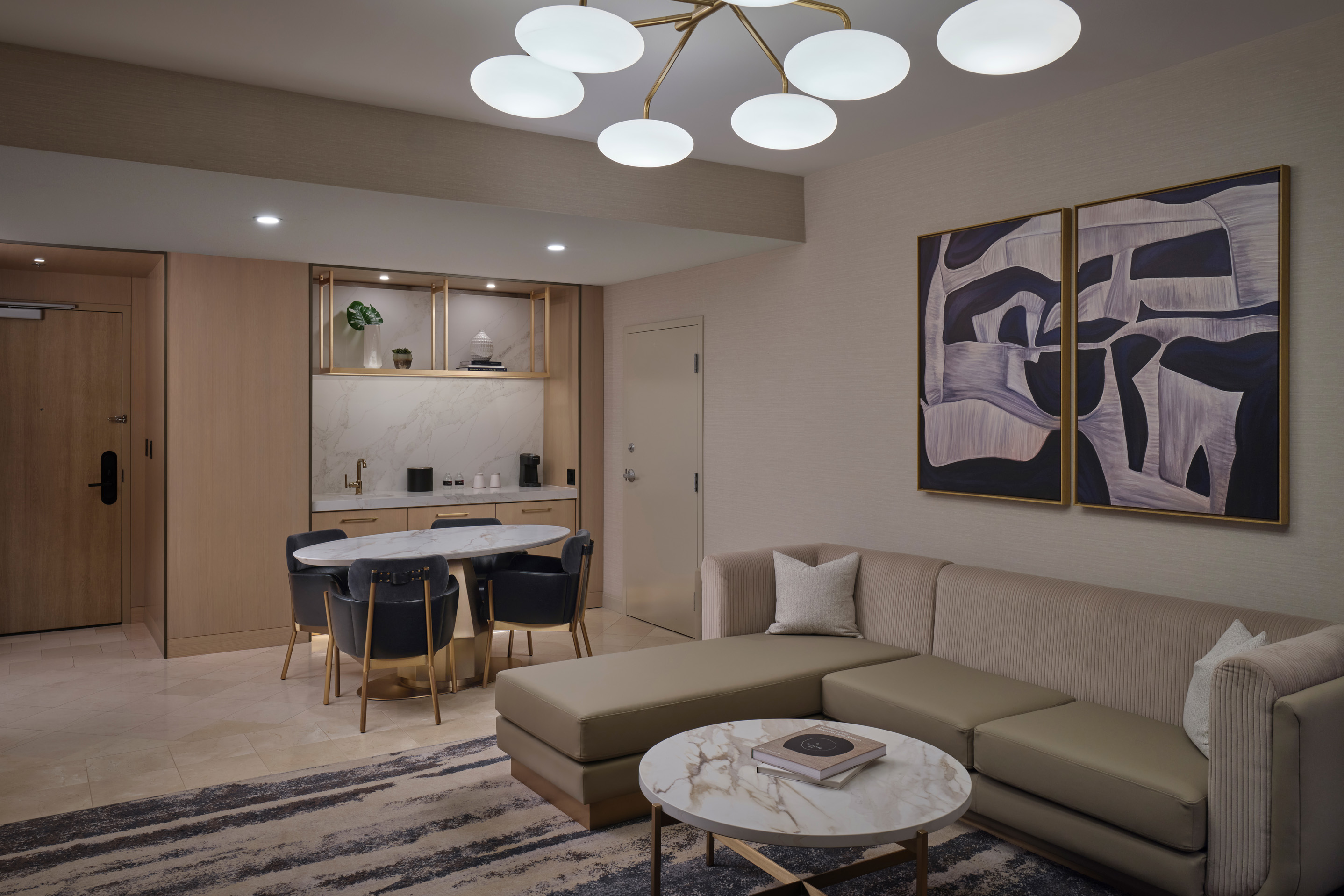 Modern hotel suite living room with dining area, lounge seating, and contemporary artwork