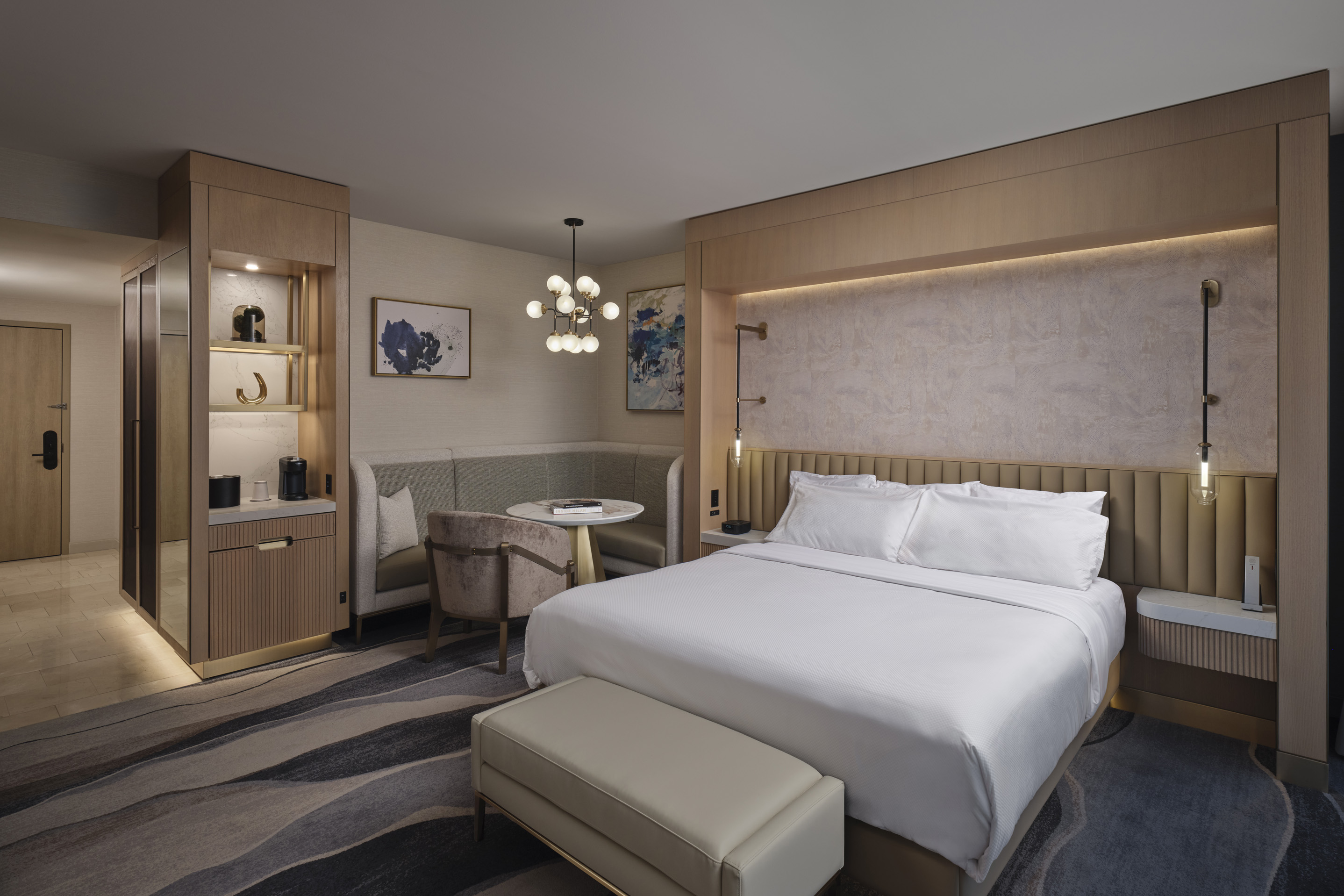 Modern luxury hotel guest room with king bed, seating area, and contemporary wood finishes
