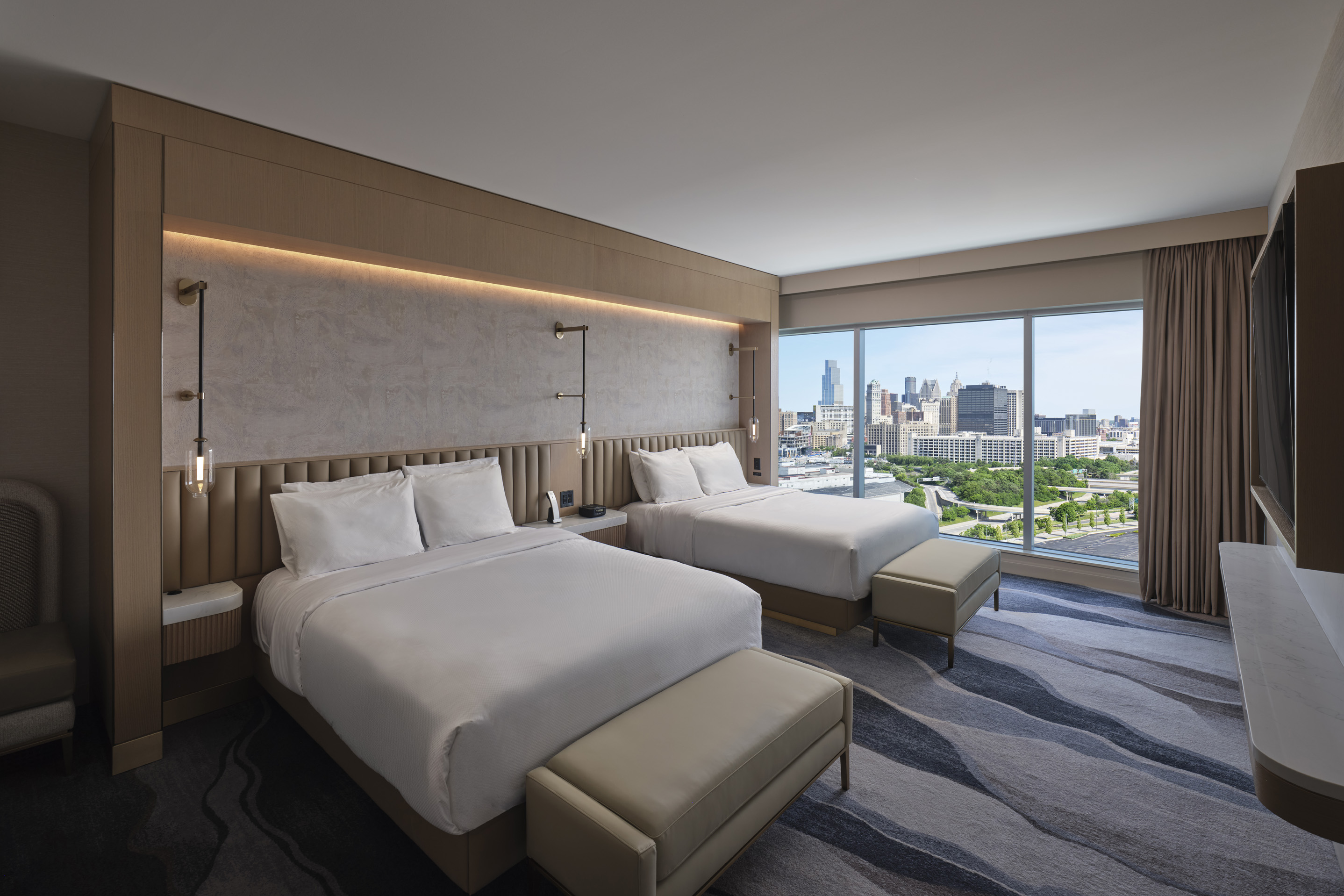 Modern king hotel room with floor-to-ceiling windows, lounge chair, and Detroit skyline views